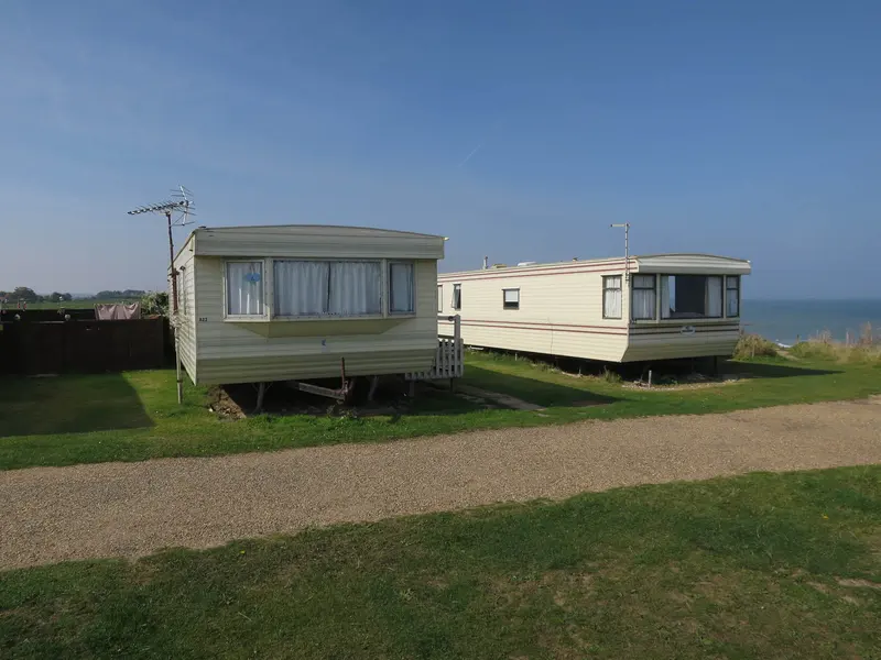 Two older static caravans on grass pitches near the coast under a blue sky