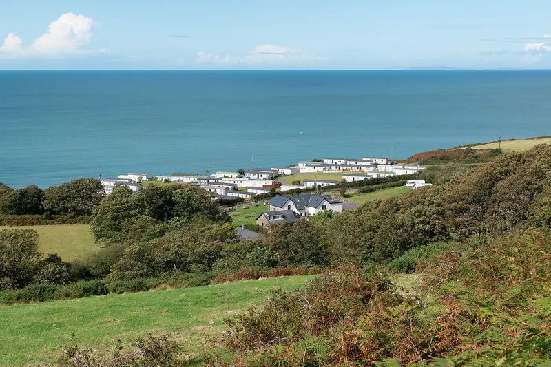 A caravan site on a green hillside above the sea, seen from higher ground