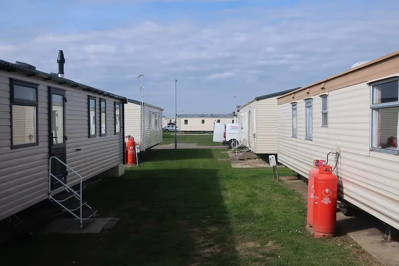 A row of static caravans on grass pitches, with steps up to the doors and a gas bottle beside one caravan